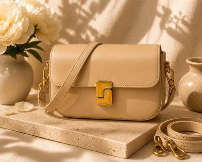 Beige handbag with gold accents on a light wooden surface with flowers and vases in the background