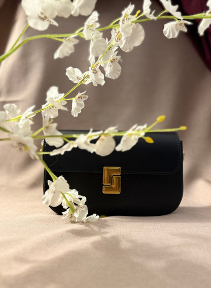 Black handbag with gold clasp on a beige surface with white flowers
