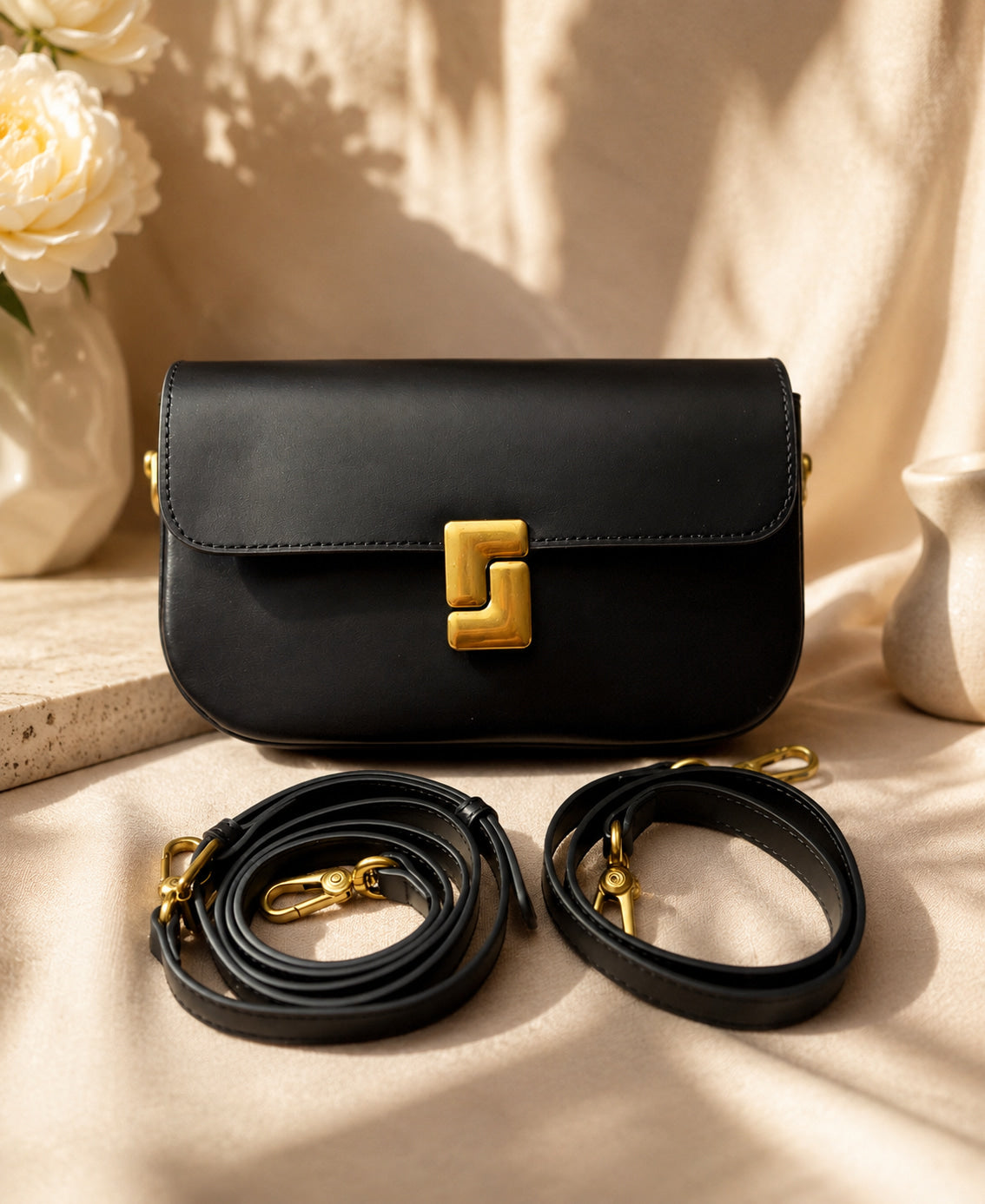 Black handbag with gold accents on a beige surface with flowers in the background