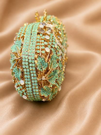 Decorative egg with green gemstones and gold accents on a beige fabric background